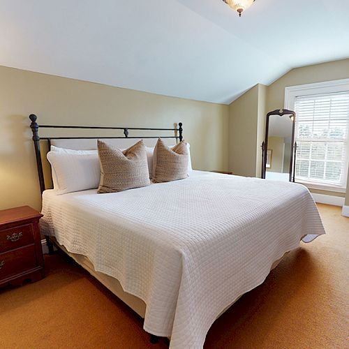 The image shows a neatly arranged bedroom with a large bed, two bedside tables with lamps, a wardrobe, and a window with blinds.