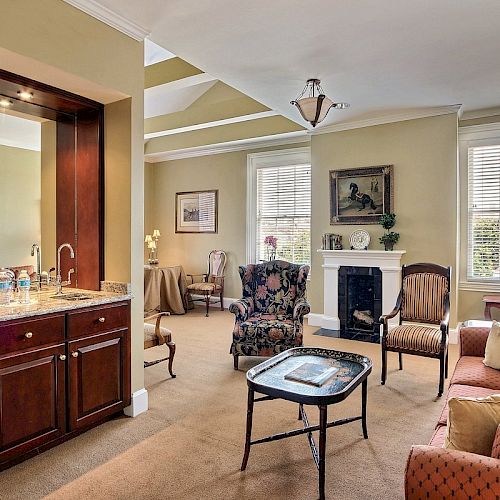 A warmly lit living area features a sofa, chairs, a table, a fireplace, and a small bar area with a sink and a TV mounted above.