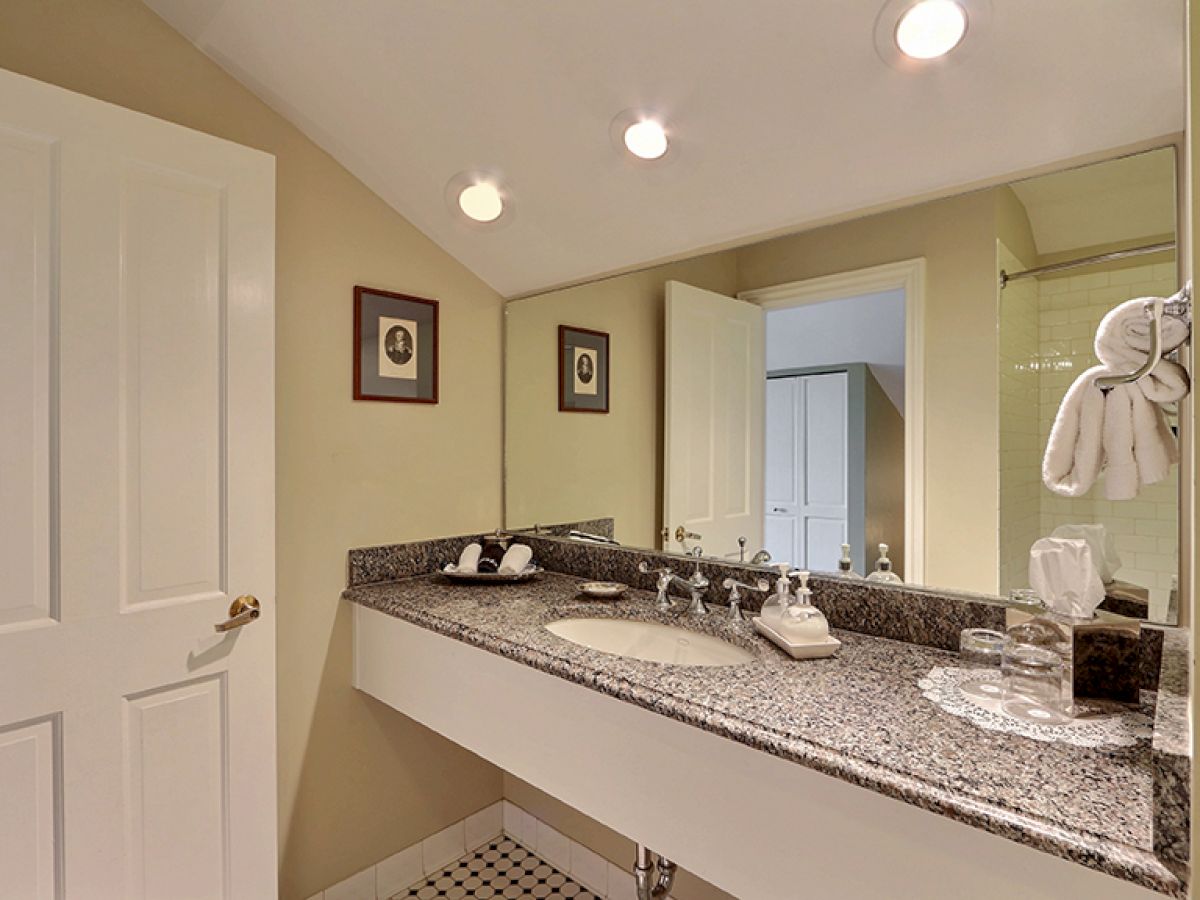 A bathroom with a granite countertop, under-mount sink, mirror, framed pictures on the wall, and a towel rack with folded towels.