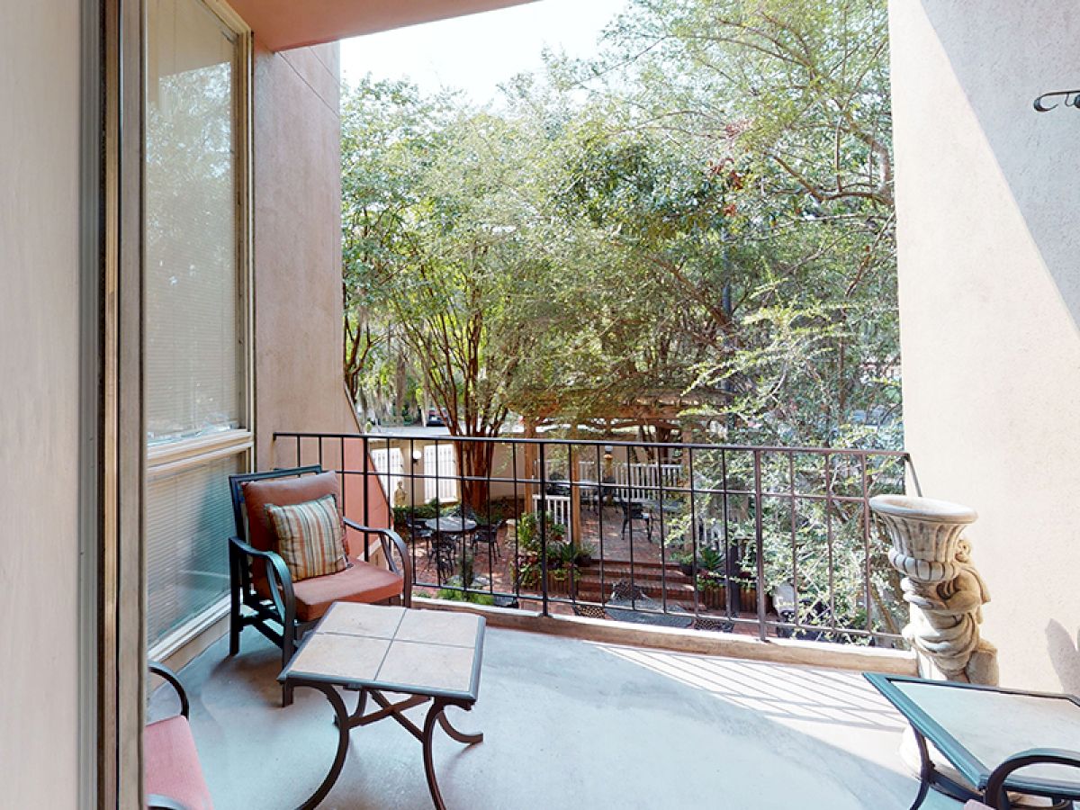 A cozy balcony with chairs and a table, bordered by a railing, overlooks lush greenery and provides a serene outdoor space.