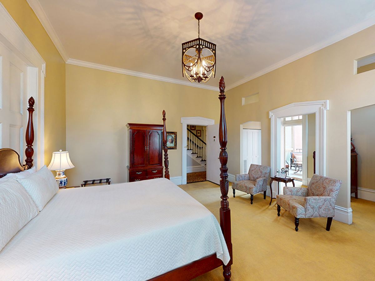 A spacious, well-lit bedroom with a large bed, seating area, chandelier, and classic furniture in a calm, neutral color scheme, ending the sentence.