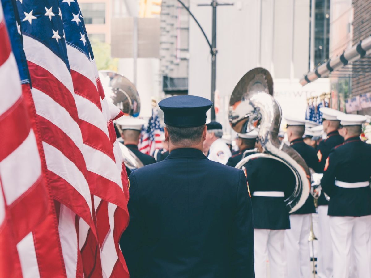 A group of uniformed individuals with American flags, some holding musical instruments, appears to be participating in a formal event or parade.