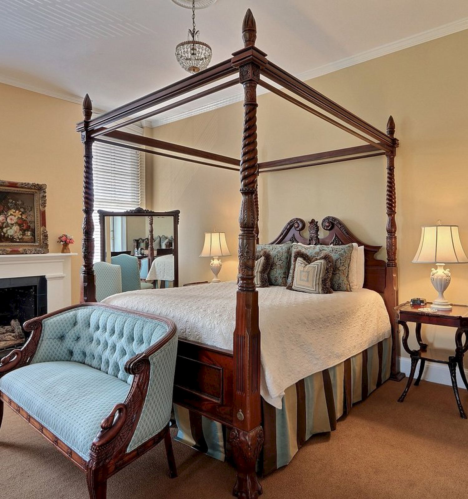 A cozy bedroom with a four-poster bed, a fireplace, a vintage chair, lamps on side tables, a mirror, and artwork on the wall.