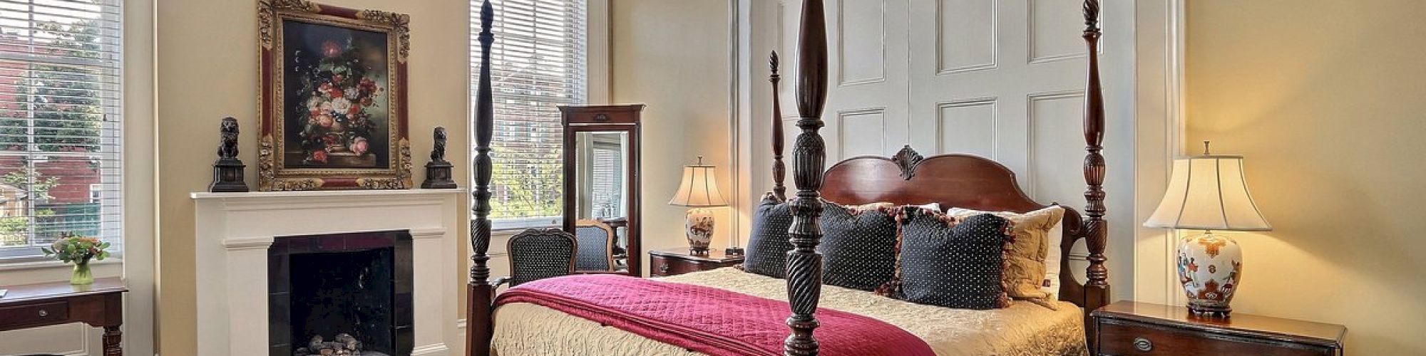 A beautifully decorated bedroom with a four-poster bed, elegant chandelier, fireplace, artwork, and wooden furniture, invoking a classic and cozy ambiance.