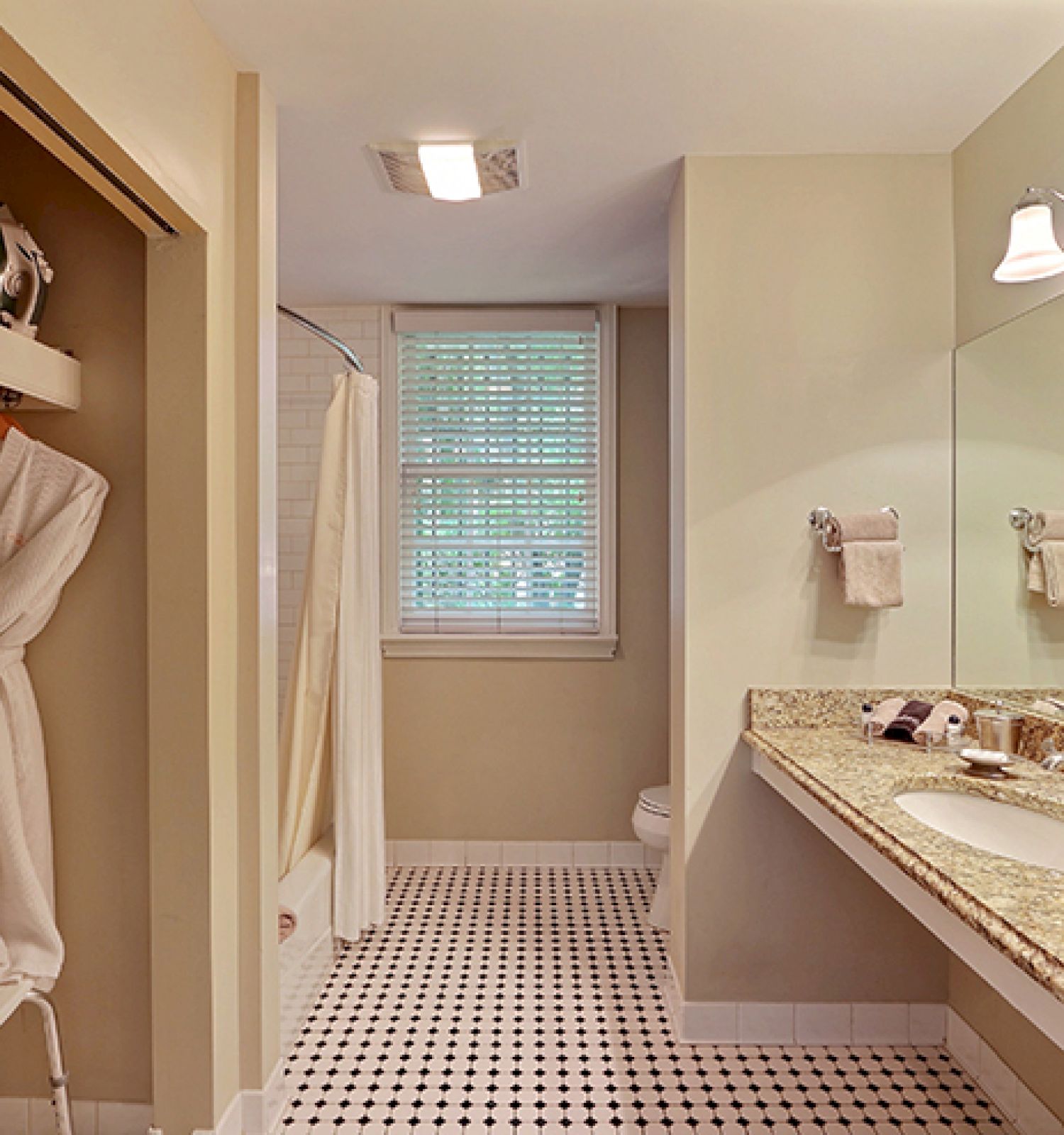 The image shows a bathroom with a shower, a sink with a large mirror, towels, and a bathrobe hanging in an adjacent closet space.