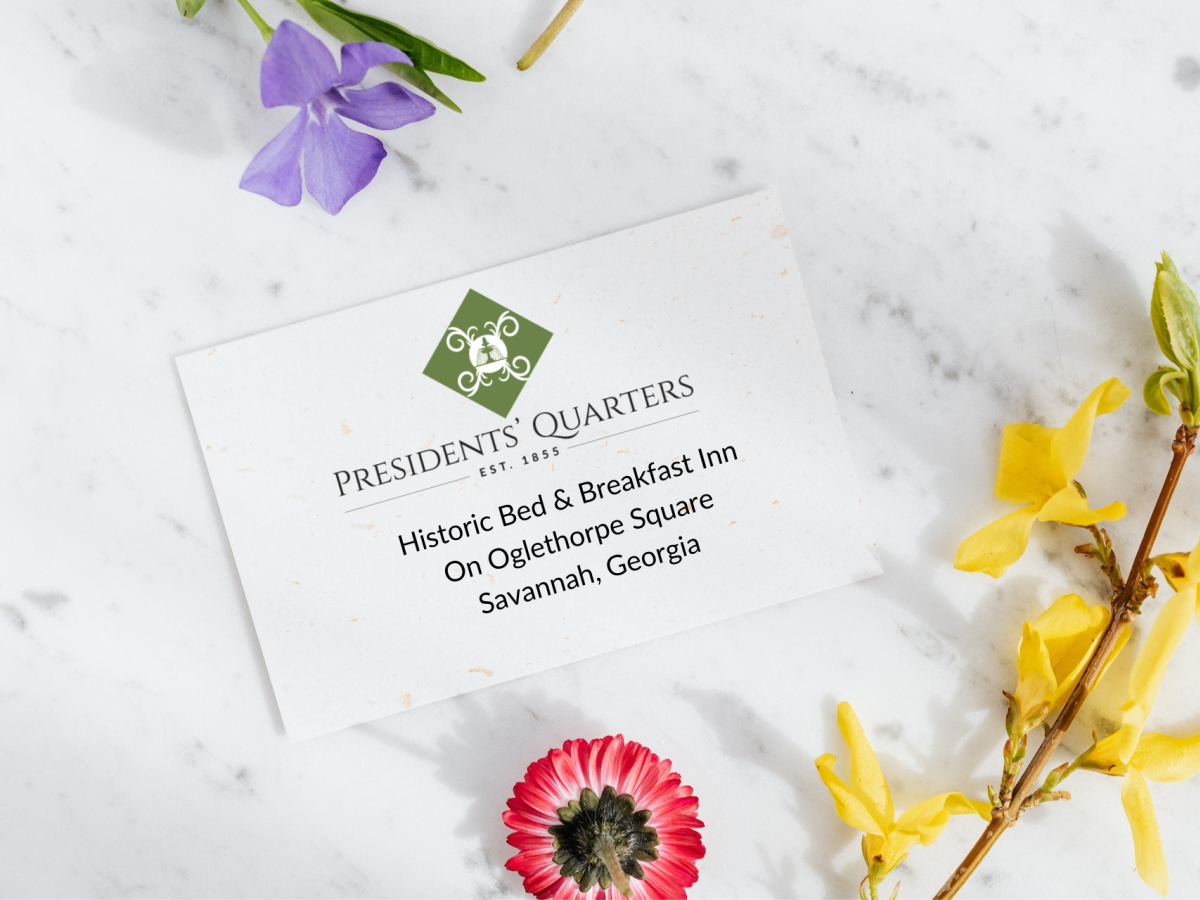 A card from President's Quarters Inn in Savannah, Georgia, is surrounded by a pink, a purple, and yellow flowers on a marble surface.